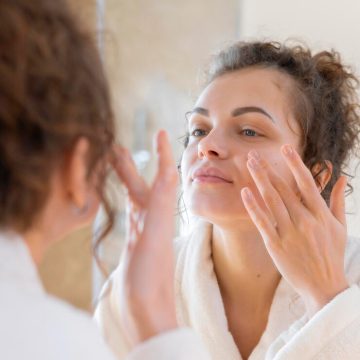 woman-applying-cream-face-while-looking-mirror